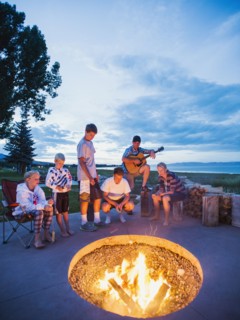 Parents with children (8-9, 10-11, 16-17) sitting in front of campfire and playing guitar