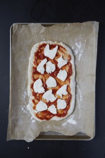 Pizza dough with tomato sauce and mozzarella on wax paper