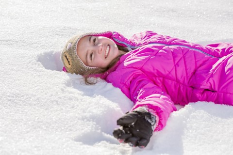 Girl (10-11) in pink jacket lying in snow