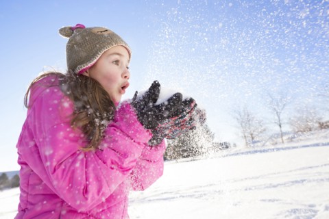 Girl (10-11) in pink jacket blowing snow