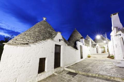 Trulli houses along illuminated street under blue sky