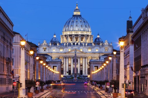 Illuminated St. Peter's Basilica with asphalt road in foreground at dusk