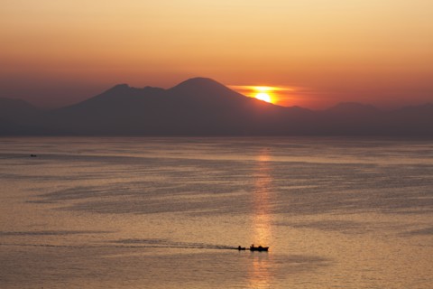 Silhouette of boat on sea with mountains in background at sunset