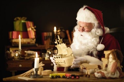 Santa Claus making wooden toy and winking.