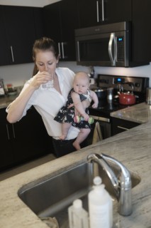Mother drinking water while holding baby daughter (2-5 months).
