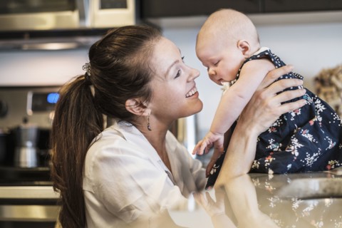 Mother playing with baby daughter (2-5 months) in kitchen.
