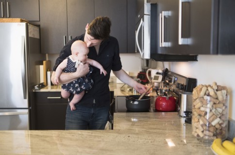 Father kissing baby daughter (2-5 months) while stirring food.