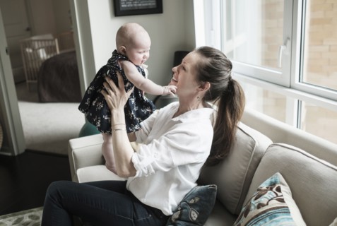 Mother playing with baby daughter (2-5 months) in living room.