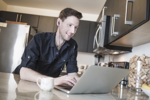 Man smiling while working on laptop computer in kitchen.