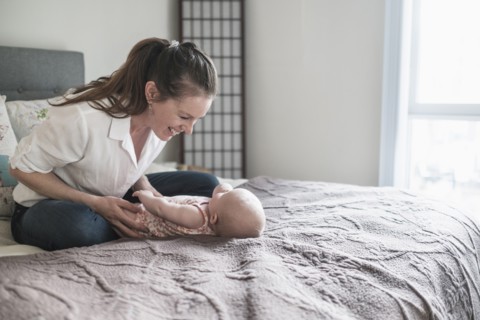 Mother playing with baby daughter (2-5 months) in bedroom.