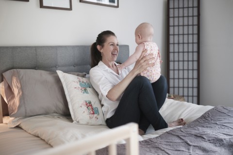 Mother playing with baby daughter (2-5 months) in bedroom.