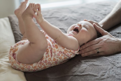 Father playing with daughter (2-5 months) on bed.