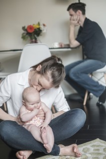 Mother holding baby (2-5 months) and father working in background.
