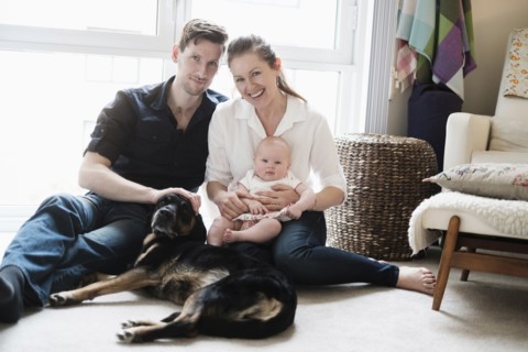 Portrait of happy family sitting on carpet with daughter (2-5 months) and dog.