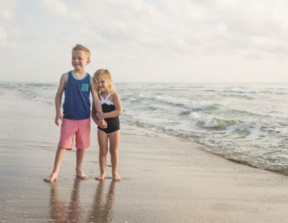 Boy (6-7) and girl (4-5) standing on beach by water holding hands