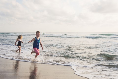 Boy (6-7) and girl (4-5) running on beach by water