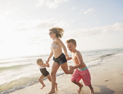 Mother running with boy (6-7) and girl (4-5) on beach by water
