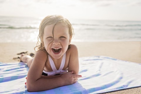 Girl (4-5) lying on beach laughing