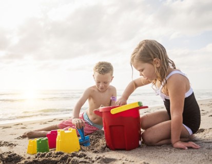 Boy (6-7) and girl (4-5) playing with sand on beach