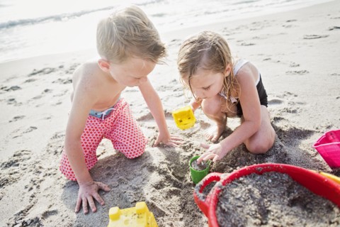 Boy (6-7) and girl (4-5) playing with sand on beach