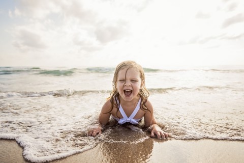 Girl (4-5) lying down in water on beach