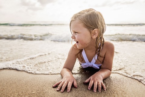 Girl (4-5) lying down in water on beach