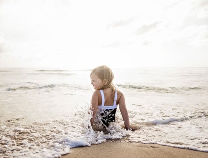 Girl (4-5) sitting in water on beach
