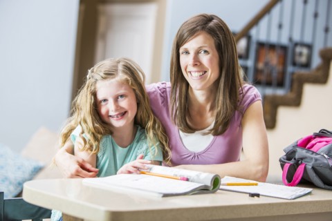 Smiling mother and daughter (8-9) sitting at table studying