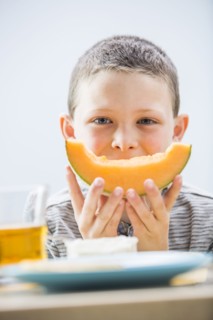 Little boy (6-7) eating cantaloupe for breakfast
