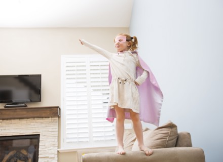 Little girl (4-5) playing superman on sofa