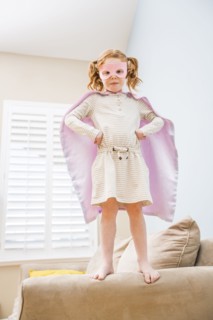 Little girl (4-5) playing superman on sofa