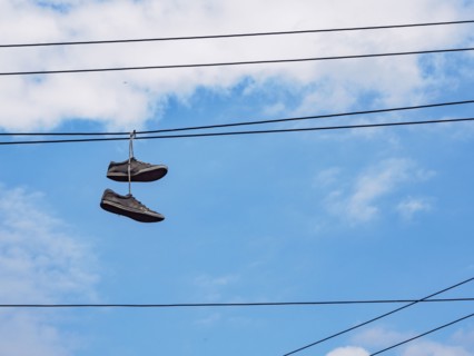 Pair of shoes hanging on cable lines against sky