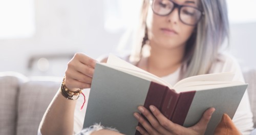 Young woman sitting on sofa and reading book.