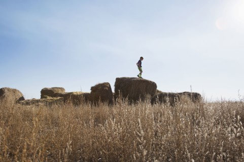 Boy (6-7) standing on bale of hay