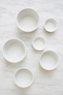 Overhead view of empty white ceramic bowls on marble table