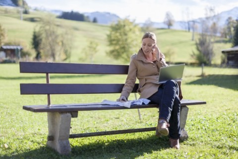 Austria, Salzburger Land, Maria Alm, Mature woman sitting on bench and talking on phone