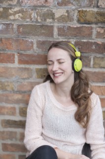 Mid-adult woman sitting and leaning against brick wall with closed eyes and headphones on