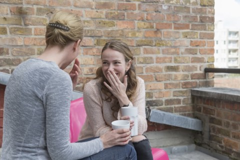 Women gossiping while sitting on balcony with coffee cups