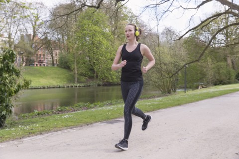 Mid-adult woman with headphones on jogging by canal in park