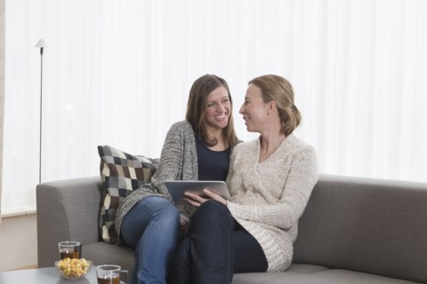 Smiling women sitting on sofa in living room and holding tablet