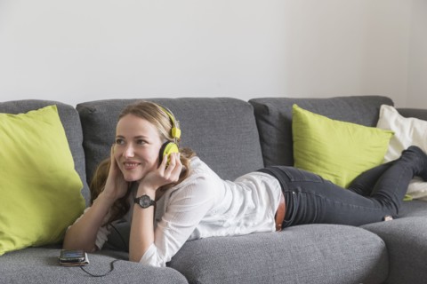Mid-adult woman lying on sofa and listening to music from smart phone