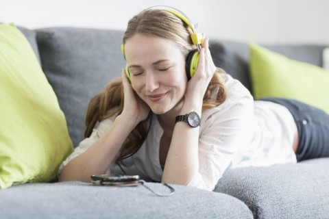 Mid-adult woman lying on sofa and listening to music from smart phone