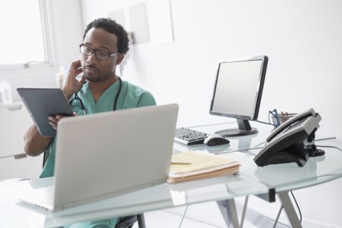 Male doctor working with digital tablet at desk.