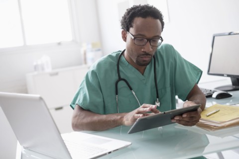 Male doctor working with digital tablet at desk.