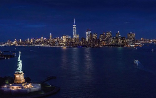 USA, New York, New York City, Manhattan, Aerial view of illuminated skyline with Statue of Liberty at night.