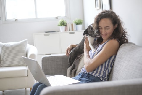 Young woman with laptop cuddling with her dog on sofa.