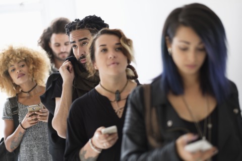 Young people standing in line using smartphones.