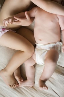 Girl (2-3) lying on bed with baby brother (6-11 months)