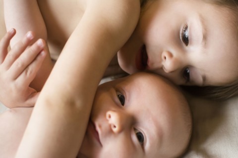 Girl (2-3) lying on bed with baby brother (6-11 months)
