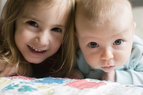 Sister (2-3) and brother (6-11 months) lying on bed and looking at camera